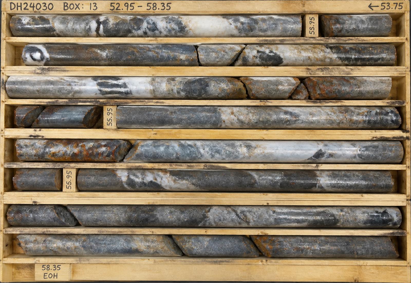 Diamond drill core in a core box showing quartz-carbonate vein material with sulphide selvages cutting dark mafic volcanic host rock